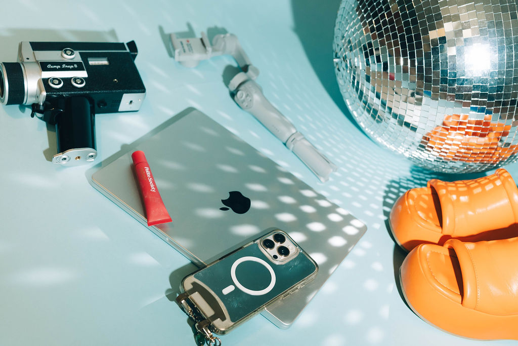 Flat lay of Morgan's content kit: a CampSnap film camera, phone gimbal, laptop and disco ball